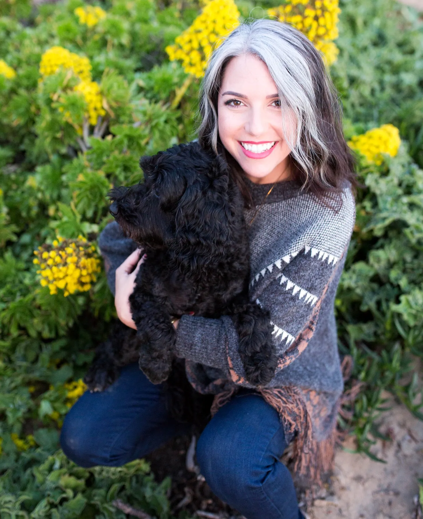 Amanda Ree, a TrueSource Global client in the US, hugging her black curly-coated dog among yellow flowers