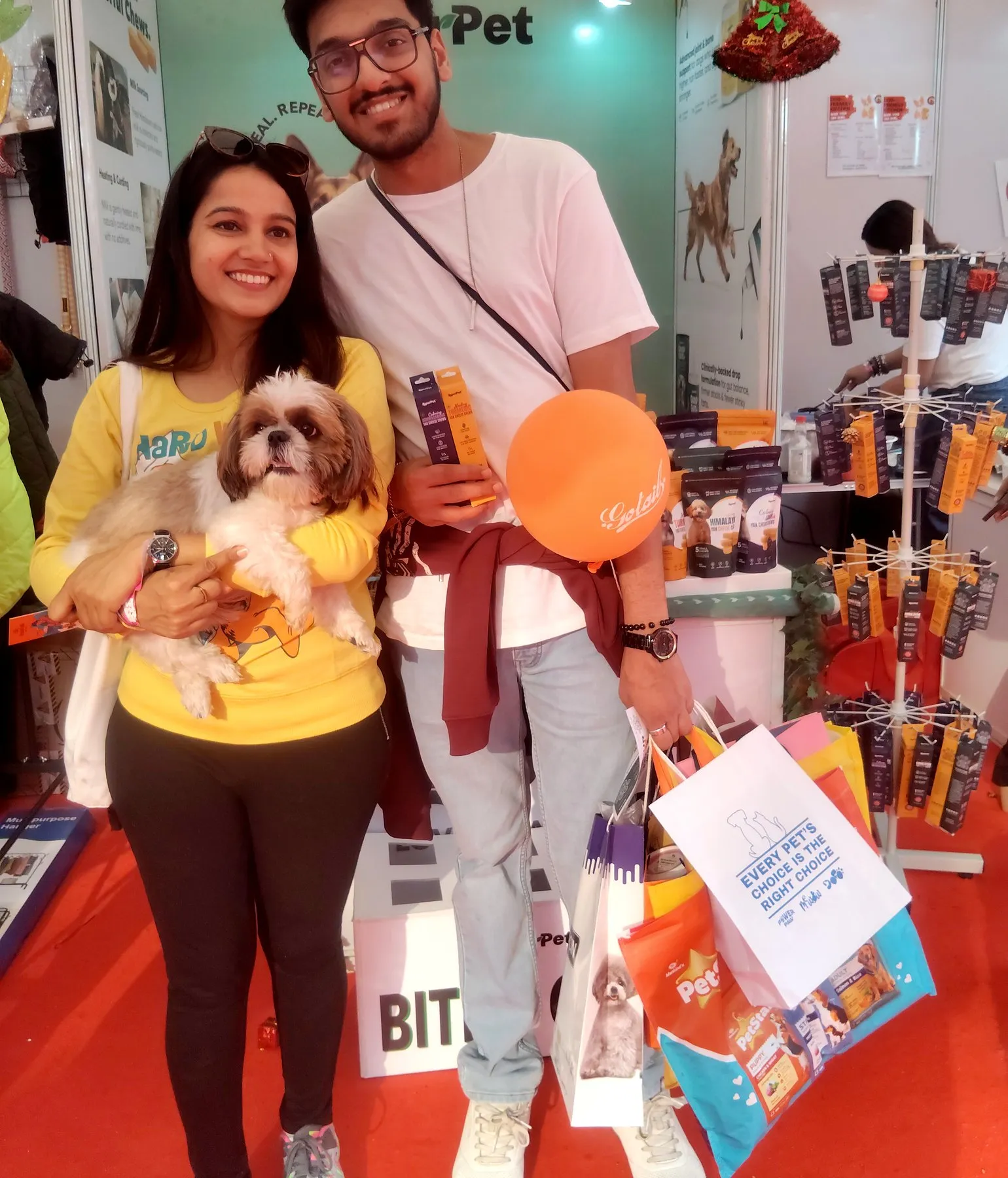 Two pet parents at an expo holding their Shih Tzu and bags of pet products